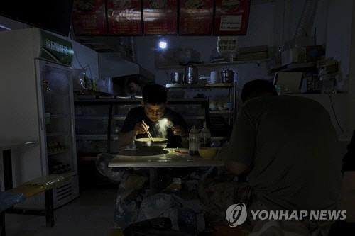 극심한 전력난을 겪고 있는 중국 북동부 랴오닝성 선양의 한 식당에서 지난 9월29일 정전사태가 빚어지자 한 남성이 휴대전화 불빛에 의지해 아침 식사를 하고 있다. <선양 AP=연합뉴스>
